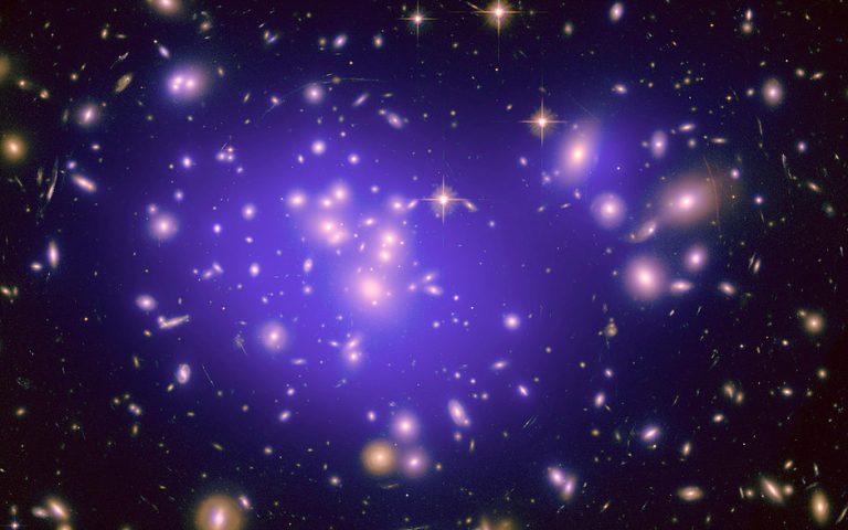 A galaxy cluster glowing with purple and surrounded by stars in deep space.